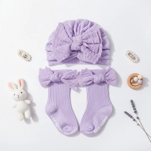 Detail view of purple knitted baby turban hat and matching bow socks on white background