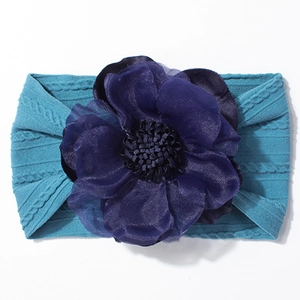 Détail d'un bandeau bébé en maille bleu paon orné d'une grande fleur violette foncée