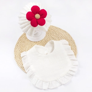 Dettaglio bavaglino bianco con volant e cappellino per neonati con grande fiore rosso