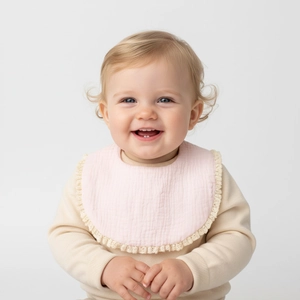 Pink cotton gauze baby bib with beige lace trim shown on an infant's beige sweater