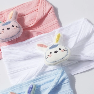 Detailed view of three knitted baby headbands in pink, white, and blue with plush bunnies