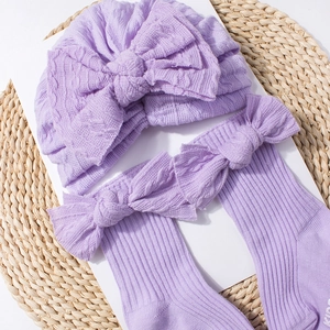 Detail of lavender knit baby hat and socks set with bows on a rustic woven mat
