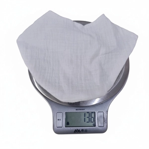 Close-up of a white cotton baby bib on a digital scale showing a light weight of 13.8g