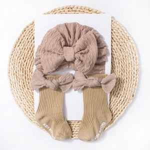 Flat lay of knit baby hat and socks set with bows on a woven mat with white background
