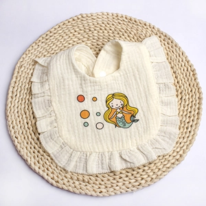 Detail of baby muslin cotton bib with ruffled edges and mermaid print on woven mat