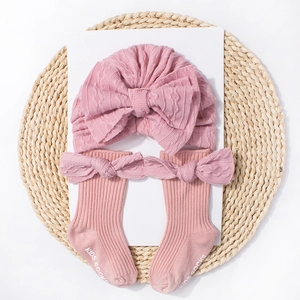 Detail of pink knitted baby hat and socks set with bows on a woven mat