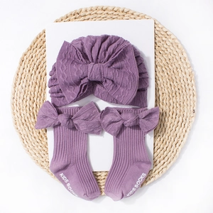 Detail of purple baby turban hat and matching socks with bow accents on a woven mat