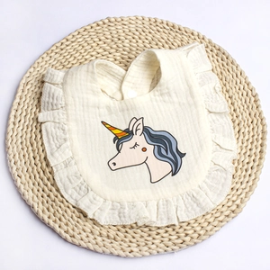 Close-up of cotton baby bib with ruffles, unicorn print, and snap button on straw mat