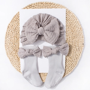 Detailed close-up of grey knitted baby turban and socks set with large bow decorations