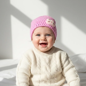 Detailed knit texture of a pink baby beanie featuring a cute cat patch and soft yarn