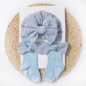 Close-up of light blue baby turban hat and matching bow socks on a woven mat base