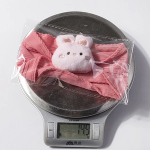 Bandeau bébé tricoté rose avec lapin en peluche blanc, posé sur une balance pour la pesée