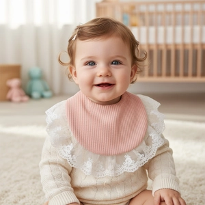 Close-up of pink cotton baby bib with delicate white lace trim on an infant model