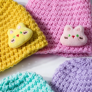 Detailed macro view of soft knit baby beanies featuring cute 3D plush animal patches