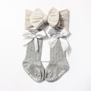 Detail of baby grey knit socks with satin bows and beige oversized bow headband
