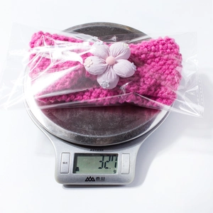 Pink knit baby headband with purple floral decor shown on a scale weighing 32.7g