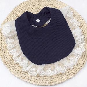 Detail shot of navy blue waffle cotton baby bib with floral lace trim and snap closure