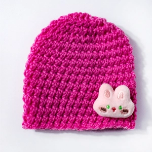 Detail of hot pink knit baby beanie featuring a soft plush rabbit patch with embroidery