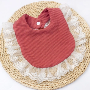 Close-up of baby bib with waffle knit texture and delicate white lace trim detail
