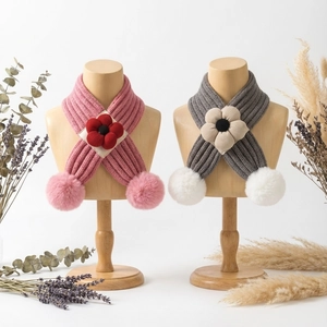 Détail d'écharpes tricotées pour bébé avec fleurs et pompons sur mannequins en bois