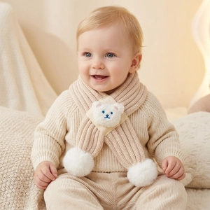 Detail of baby beige knit scarf featuring cute bear patch and soft white pom-poms