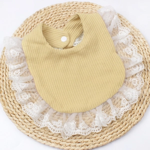 Detail of baby mustard yellow waffle bib with delicate white lace trim and button closure