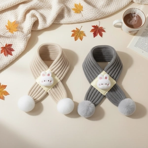Close-up of baby knitted scarves with plush rabbit decor and pom-poms on autumn background
