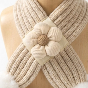 Détail d'une écharpe bébé en grosse maille beige avec fleur décorative et pompons doux