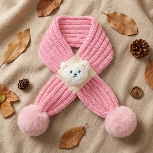 Pink knitted baby scarf with plush bear patch and large pom-poms on beige linen background