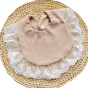Detailed view of beige waffle fabric baby bib with white lace trim and button snap