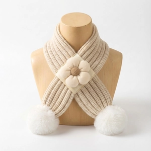 Détail d'une écharpe tricotée beige pour bébé avec fleur 3D et pompons blancs doux