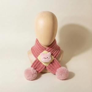 Close-up of pink knitted baby scarf featuring a cute plush pig and fluffy pom-poms