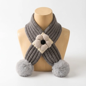 Détail d'une écharpe en tricot gris pour bébé avec fleur en tissu et pompons en peluche doux