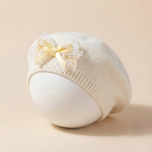 Détail du béret en tricot pour bébé avec nœud en dentelle jaune et petites perles blanches