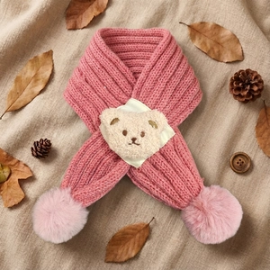 Detail of pink knitted baby scarf with bear patch and fluffy pom-pom decorations