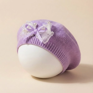 Détail d'un béret tricoté violet pour bébé avec un nœud en dentelle et des perles fines