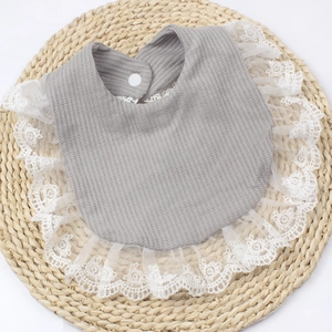 Detail of baby bib with grey waffle cotton fabric, white lace trim and secure snap button