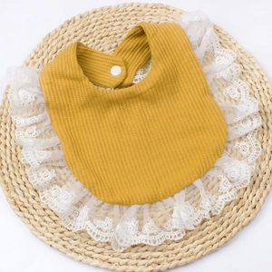 Detail of baby bib showing mustard yellow waffle fabric texture and white lace trim