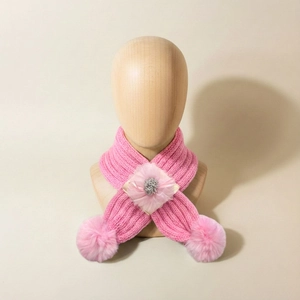 Détail d'une écharpe tricotée rose pour bébé avec fleur en résille et pompons