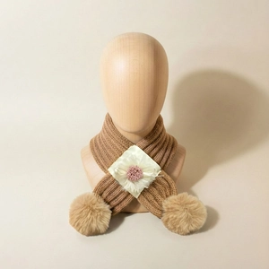 Détail d'écharpe en tricot bébé avec fleur blanche et pompons marrons sur support bois