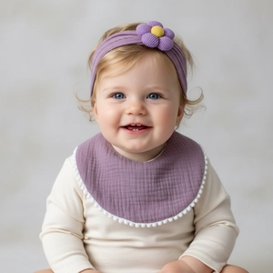 Detail of purple muslin baby bib with white pom-poms and matching flower headband