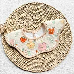 Floral cotton muslin baby bib with petal edges and snap fastener on a woven mat