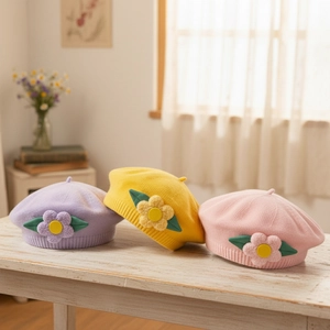 Knitted baby flower beret in pastel colors with handmade floral detail on white wood