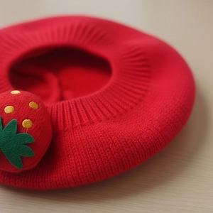 Béret tricoté pour bébé rouge avec décoration fraise sur fond de bois clair naturel