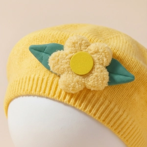 Infant yellow knit beret hat with a 3D flower detail and green leaves on pink background