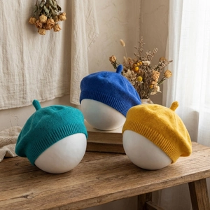 Minimalist knitted baby beret hats in blue and mustard on wooden display