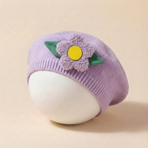 Detail of purple knit baby beret with a 3D plush flower and green leaves on a soft texture