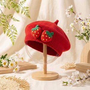 Béret tricoté rouge pour bébé avec des motifs de fraises crochetées sur support bois