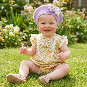 Infant girl wearing a purple knit flower beret and yellow floral bodysuit on green grass