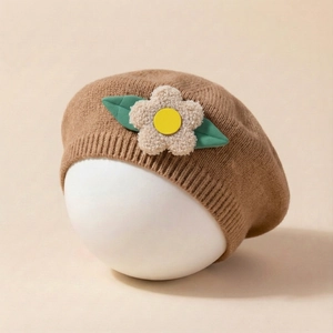 Detailed texture of brown knit baby beret with a 3D plush flower and green leaf decor